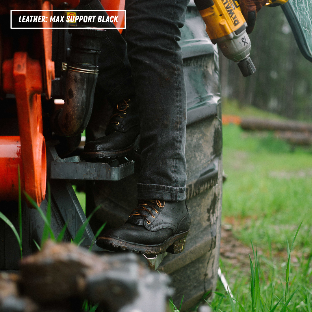 A close-up outdoor shot of a person wearing black leather work boots with orange laces, standing on the steps of a tractor next to a large tire. A yellow DeWalt cordless drill is held in the person's hand, and a text overlay in the top-left corner reads 'LEATHER - MAX SUPPORT BLACK'.