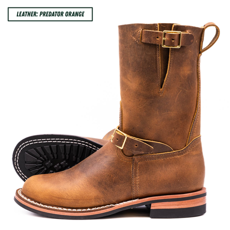 A pair of distressed leather mid-calf boots in a warm brown shade, featuring gold-tone buckles, white contrast stitching, and black soles. A text label in the top left corner reads 'LEATHER: PREDATOR ORANGE'.