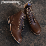 A pair of dark cognac brown leather lace-up ankle boots with brass eyelets and white contrast stitching, displayed on a dark textured background with a text label in the top left corner.