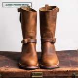 A pair of mid-calf leather boots in a distressed brown shade, styled on top of a vintage leather suitcase against a plain light background. A text label in the top-left corner reads 'LEATHER: PREDATOR ORANGE'.