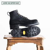 All black leather boots with lug soles. Boots sitting on wooden table, one laying down showing outsole and the other sitting side profile on top. Top left reads "LEATHER: MAX SUPPORT BLACK."