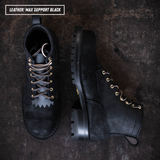 All black leather boots with lug soles. Boots sitting on textured concrete. Top left reads "LEATHER: MAX SUPPORT BLACK."