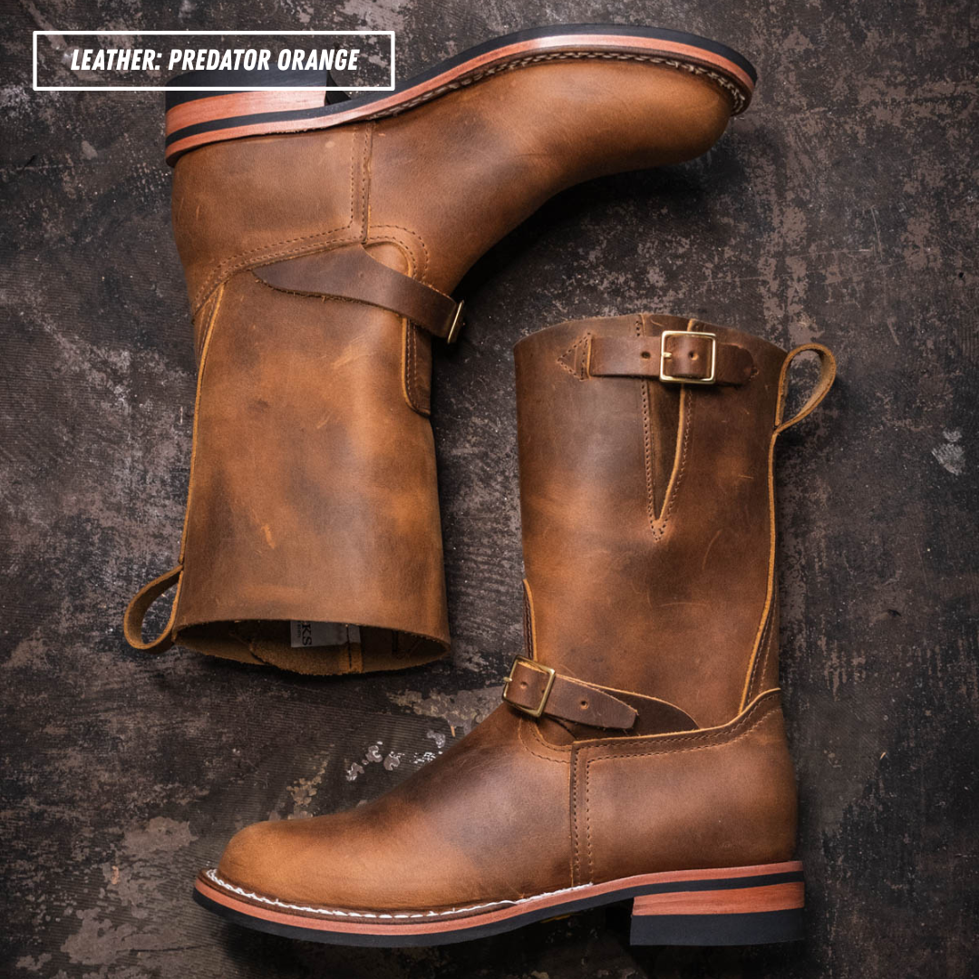Two mid-calf leather boots in a distressed brown finish, displayed on a dark textured concrete background. One boot is shown from the side profile with a strap detail, and the other is angled to show the front and heel.