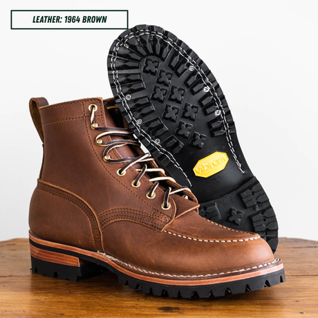 A brown leather lace-up work boot shown on a wooden surface with the outsole displayed behind it. Text in the top left reads 'LEATHER: 1964 BROWN'.