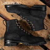 A pair of black leather lace-up boots with gold-tone metal eyelets, displayed on a rustic wooden surface. One boot is positioned above the other, showing the side profile and the top of the other boot.