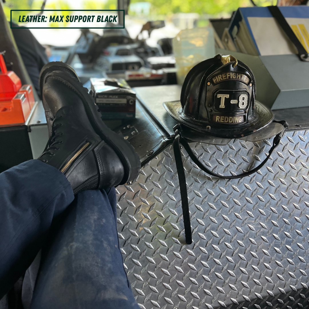 A person's legs are crossed with one foot resting on a black leather firefighter boot, while a black firefighter helmet sits on a diamond plate metal surface nearby. A text overlay in the top left reads 'LEATHER: MAX SUPPORT BLACK'.