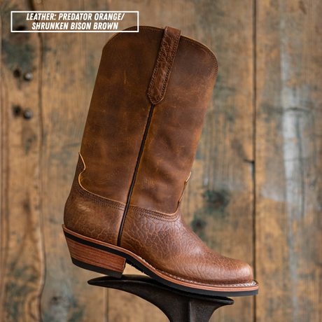Palouse western boot sitting on boot jack in front of wooden backdrop. Top left reads 'LEATHER: PREDATOR ORANGE/ SHRUNKEN BISON BROWN'.