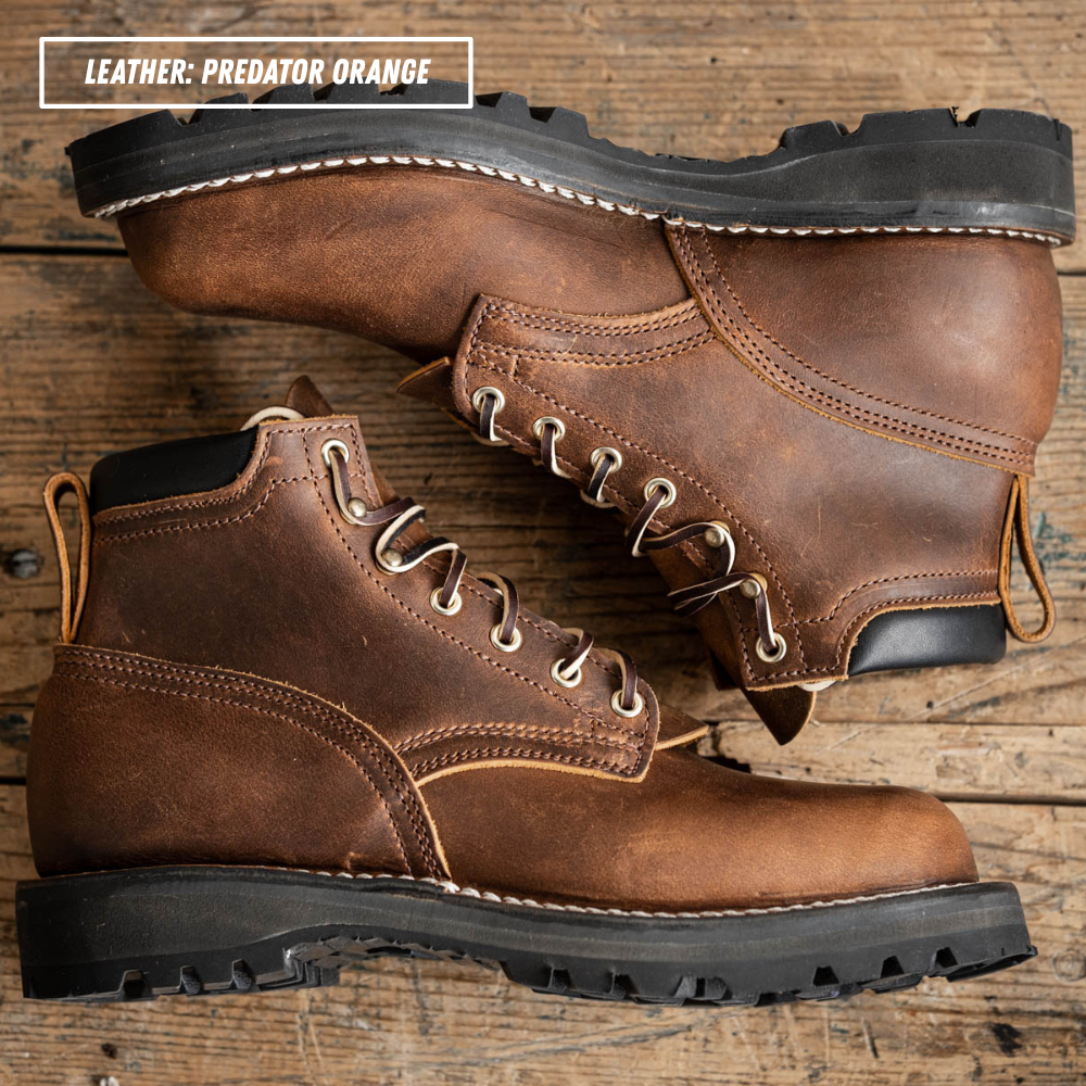 A pair of rugged lace-up work boots in distressed brown leather, arranged on a rustic wooden surface. One boot is positioned above the other, showing the side profile, toe, laces, and pull tabs.