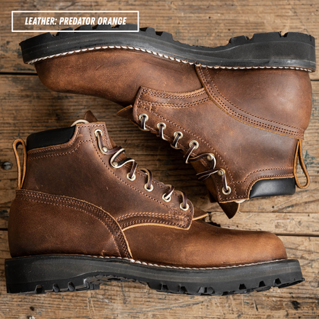A pair of rugged lace-up work boots in distressed brown leather, arranged on a rustic wooden surface. One boot is positioned above the other, showing the side profile, toe, laces, and pull tabs.