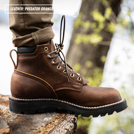 A close-up of a brown leather lace-up boot worn with cuffed brown pants, standing on a log outdoors. A text overlay in the top left reads 'LEATHER: PREDATOR ORANGE'.