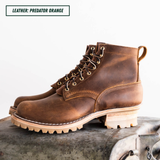 A pair of rugged lace-up ankle boots in distressed brown leather, displayed on a vintage metal trunk against a white background. A text label in the top left reads 'LEATHER: PREDATOR ORANGE'.