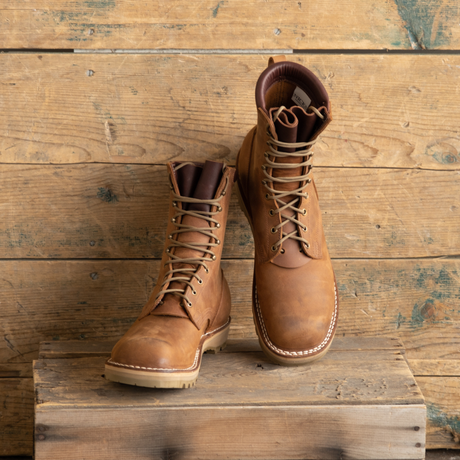 A pair of tan leather lace-up work boots displayed on a rustic wooden crate against a weathered wood plank background.