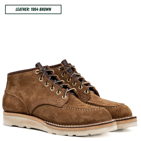 A pair of men's brown suede ankle boots with dark brown laces, metal eyelets, and a thick off-white sole, shown on a white background with a text label reading 'LEATHER: 1964 BROWN'.