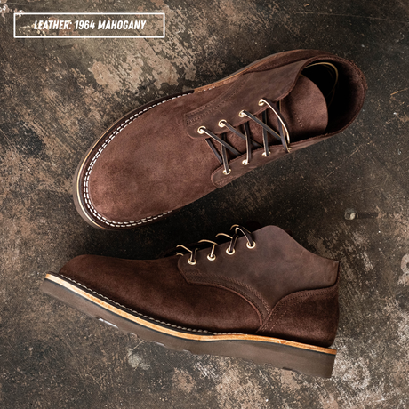 Two dark brown suede lace-up shoes arranged on a textured dark surface. One shoe is shown from the side/top and the other from the bottom/side.