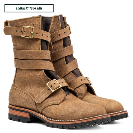 A pair of mid-calf leather boots in tan leather with multiple wrap-around straps and brass-tone buckles, shown on a white background with a small label reading 'LEATHER: 1964 TAN'.