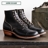A pair of black leather lace-up ankle boots with gold-toned eyelets and contrast stitching, displayed on a dark surface with a vintage green object in the background. A text box in the top left reads 'LEATHER: CXL BLACK'.