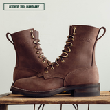 A pair of brown leather lace-up boots with gold-tone eyelets and pull tabs, displayed on a wooden surface against a light background. A text label in the top left reads 'LEATHER: 1964 MAHOGANY'.