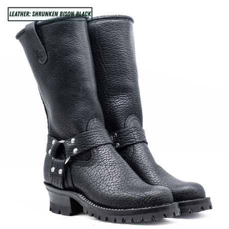 A pair of black leather mid-calf boots with a pebbled texture, featuring a buckle strap detail on the side and a rugged lug sole, shown against a plain white background.