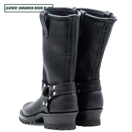 A pair of black leather mid-calf boots with a pebbled texture, featuring a decorative strap with silver studs on the side and a rugged sole, shown against a plain white background.