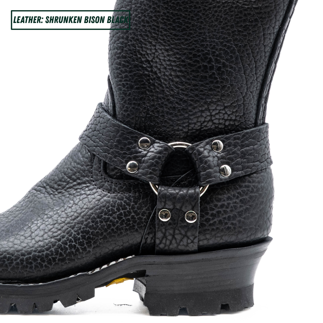 Close-up of a black textured leather boot with a buckle strap and metal studs, on a white background. A text label in the top-left corner reads 'LEATHER: SHRUNKEN BISON BLACK'.