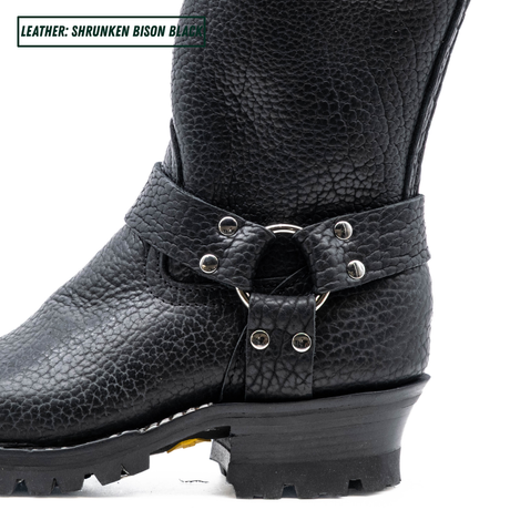 Close-up of a black textured leather boot with a buckle strap and metal studs, on a white background. A text label in the top-left corner reads 'LEATHER: SHRUNKEN BISON BLACK'.