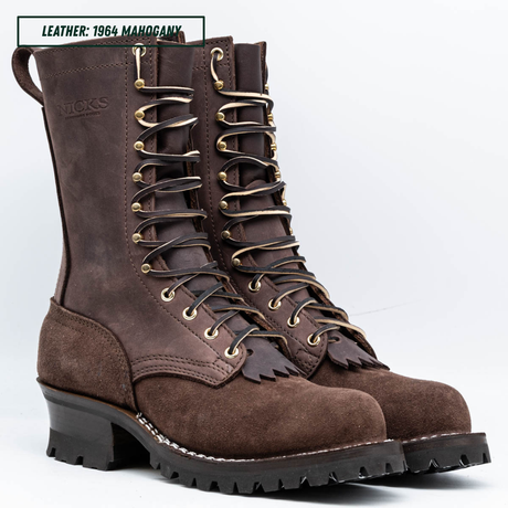 A pair of high-top brown leather lace-up boots with gold-toned metal eyelets and a chunky black lug sole, shown on a white studio background. A text label in the top-left corner reads 'LEATHER: 1964 MAHOGANY'.
