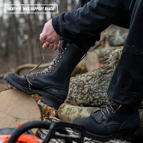 A person outdoors wearing a black leather lace-up boot and tying the laces, with another black boot on the other foot. Logs and a blurred forest background are visible, with a text overlay reading 'LEATHER: MAX SUPPORT BLACK' in the top left corner.