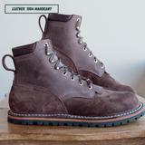 A pair of dark brown suede and leather lace-up boots on a wooden surface against a light background, with a text label reading 'LEATHER: 1964 MAHOGANY' in the top left corner.