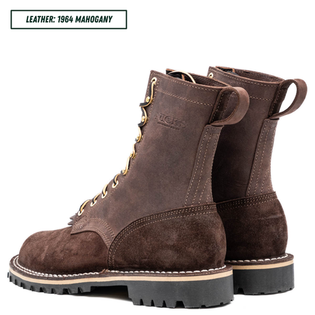 A pair of dark brown suede and leather lace-up boots shown on a white background, with a text label in the top-left corner reading 'LEATHER: 1964 MAGOGANY'. The boots feature gold-tone eyelets, white contrast stitching, and black lug soles.