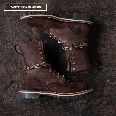 A pair of dark brown suede and leather lace-up boots arranged on a dark rustic wooden surface. The top-left corner includes a text label reading 'LEATHER: 1964 MAGOHAGNY'.