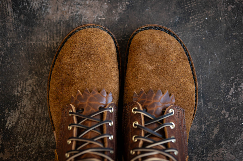 Top-down view of tan suede leather boots with lace-up dark brown leather vamps and kiltie details