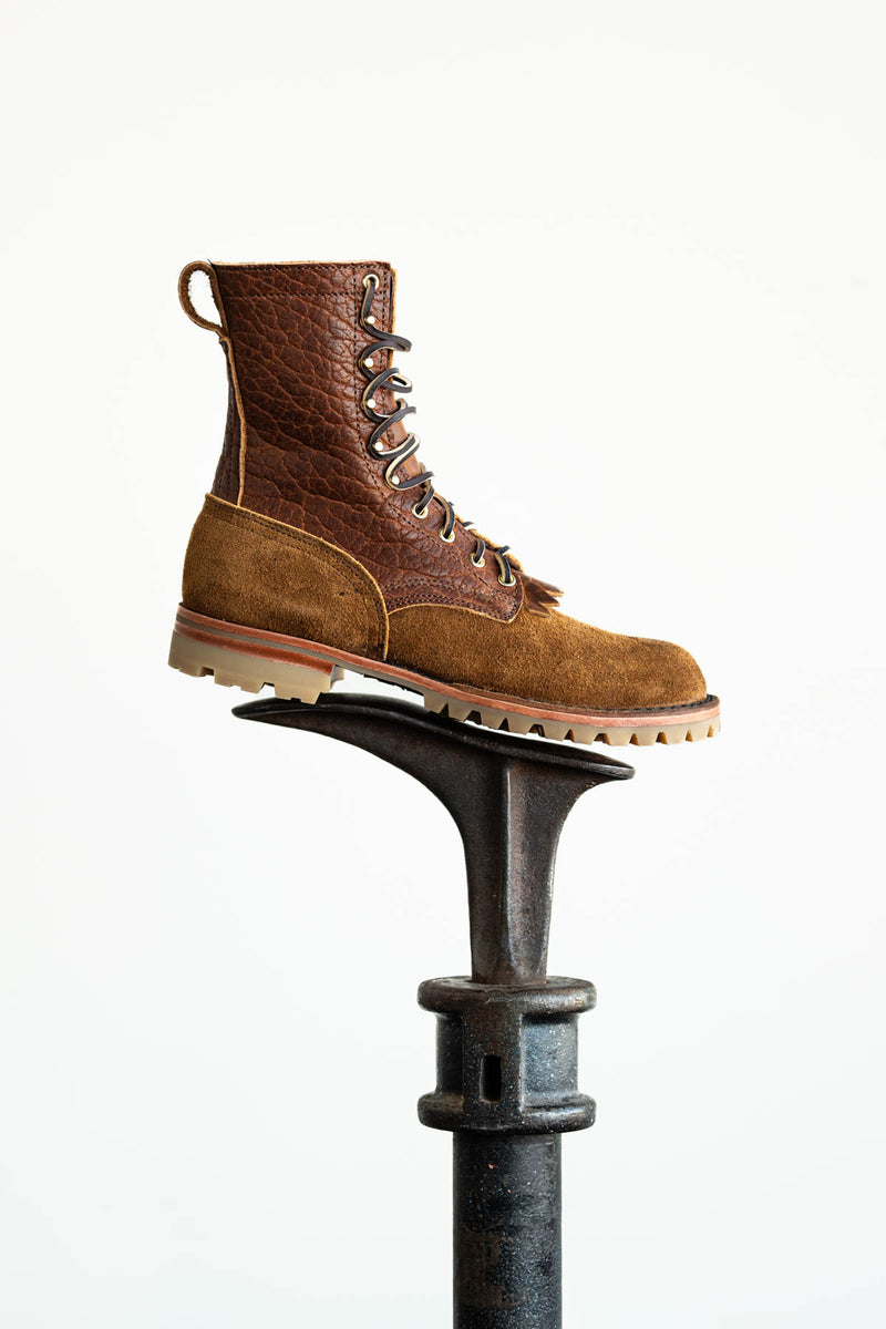 Brown textured leather and suede lace-up work boot resting on an iron shoe anvil against a white background