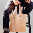 Model holding Veg Tan Suede Tote in front of white background and sitting on wooden stool.