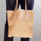 Model holding Veg Tan Suede Tote with no pocket, showing cattle brand.