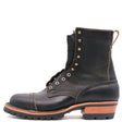 A single black leather lace-up boot with brass eyelets, a pull loop, and a stacked lug sole, shown from a side profile on a white background.