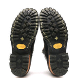 A pair of black boots shown from the sole side, displaying deep lugged rubber tread, contrast stitching, and yellow Vibram logos on the soles against a white background.