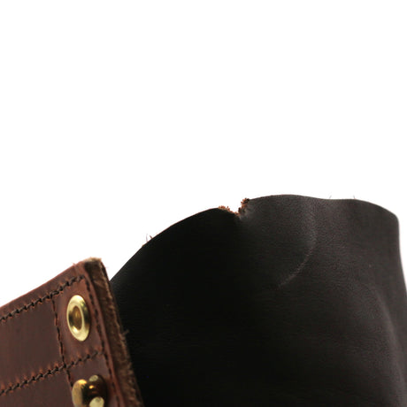 Close-up detail of a dark brown leather strap or cuff with brass-tone rivets and a black interior lining, shown against a plain white background.