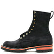 A black suede lace-up boot with gold-tone eyelets and a thick black sole featuring a vibrant orange accent stripe, shown against a plain white background.