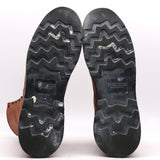 A pair of black rubber boots with a zigzag tread pattern, showing the sole and the brand name 'NICKS' molded into the rubber. The brown leather upper is partially visible on the left.