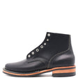 A black leather lace-up ankle boot with silver metal eyelets, a stacked black sole, and a tan leather midsole, shown from a side profile on a white background.
