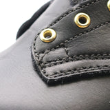 Close-up of a black leather shoe upper with gold-tone metal eyelets and detailed stitching.