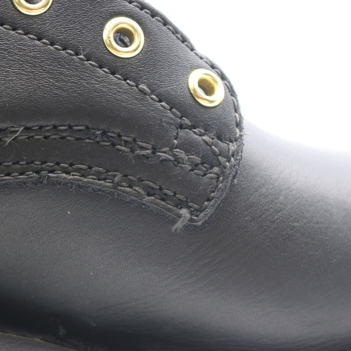 Close-up of a black leather boot showing the side panel with gold-tone metal eyelets and stitching.