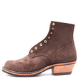 A dark brown suede ankle boot with decorative brass-tone eyelets, a stacked wood-look block heel, and contrast stitching, shown against a plain white background.