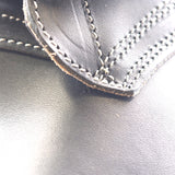 Close-up of black leather with white contrast stitching along a folded edge, showing the texture and construction detail.