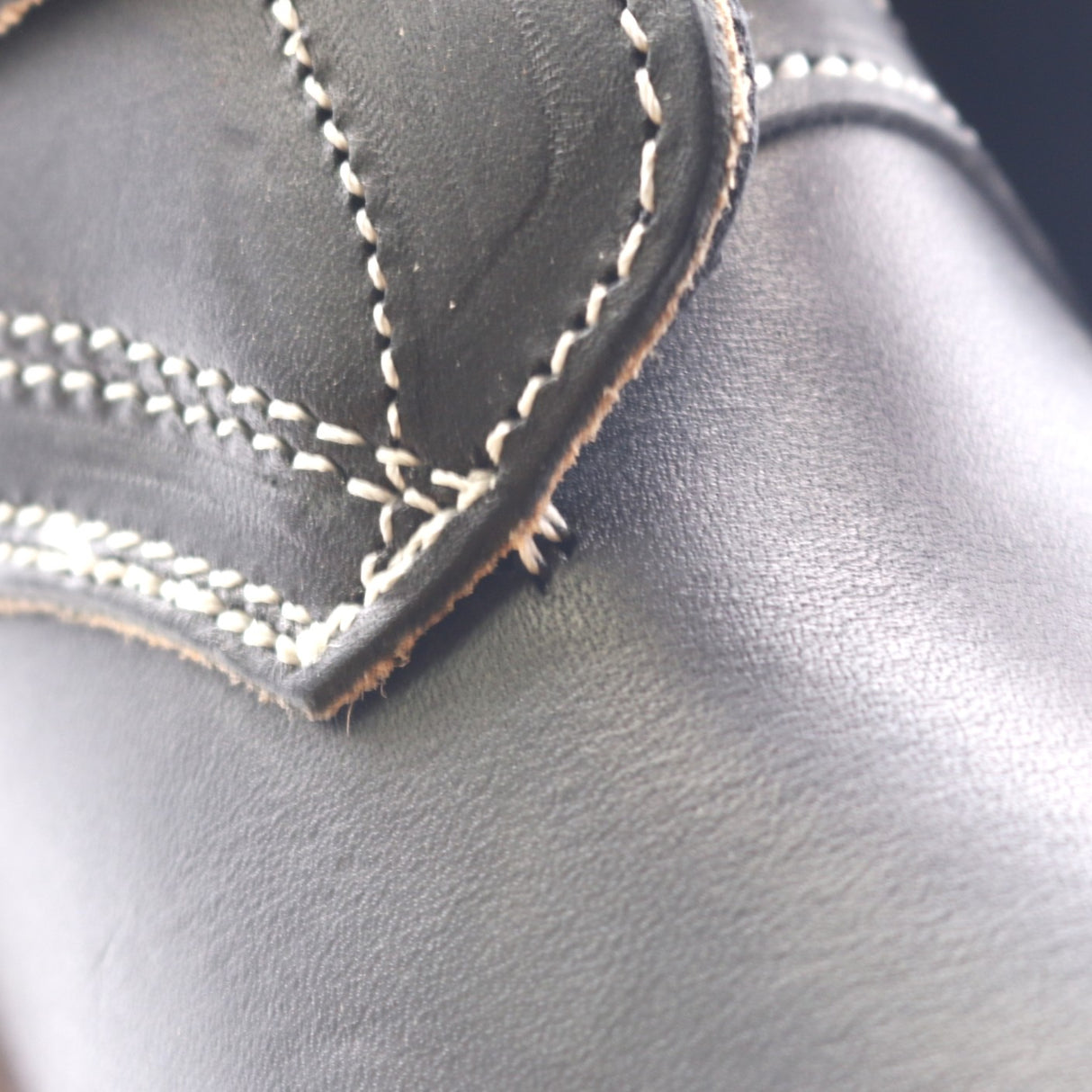 Close-up of black leather with white contrast stitching along a curved seam.
