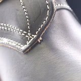 Close-up of black leather with white contrast stitching along a curved seam.