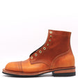 A single leather ankle boot in a warm cognac brown, featuring brass grommets, a cap toe, and a black sole, photographed against a plain white background.