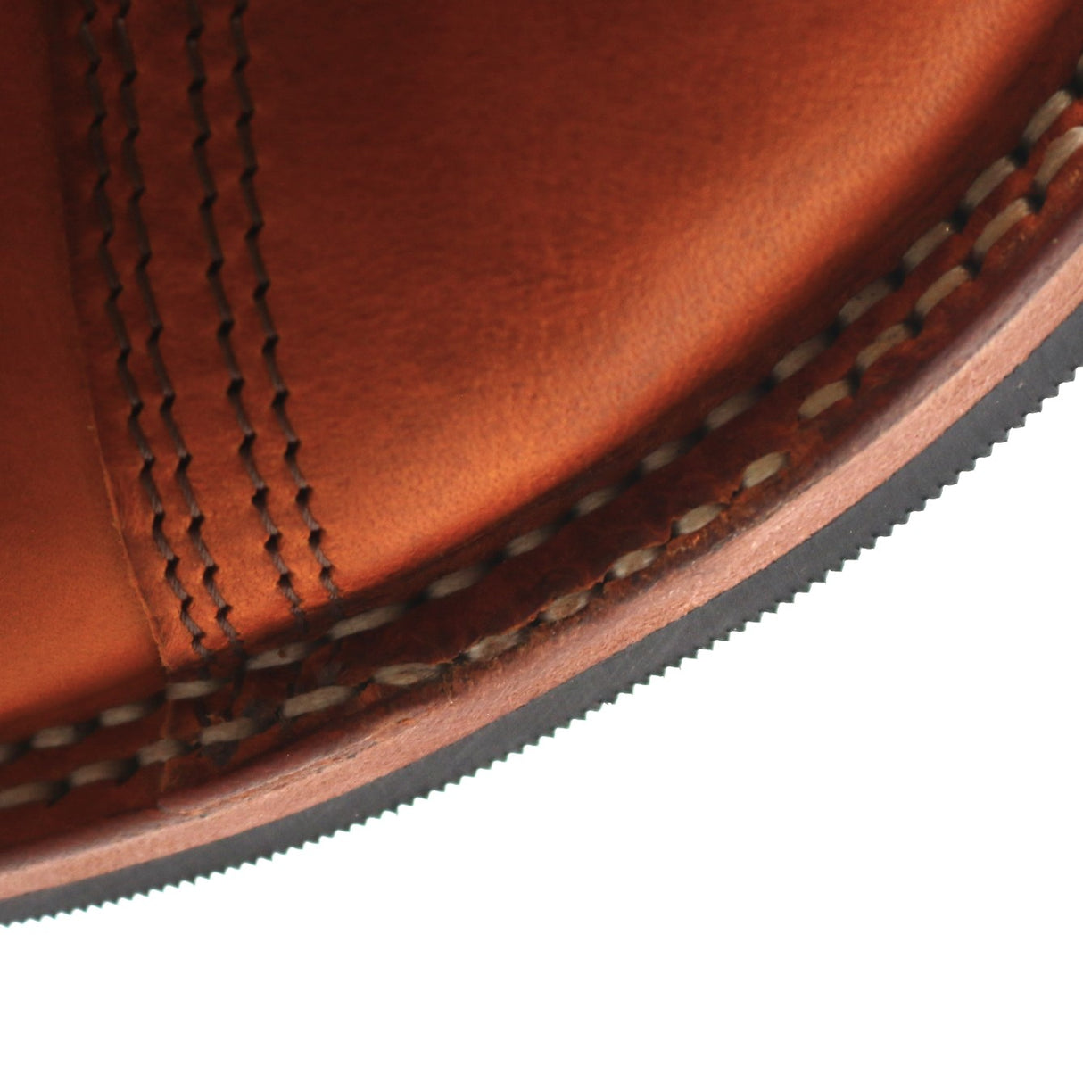 Close-up detail of a brown leather shoe corner showing double stitching, welt construction, and the edge of the sole against a white background.