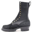 Tall black work boot with a lug outsole and brass hardware in front of a white background.