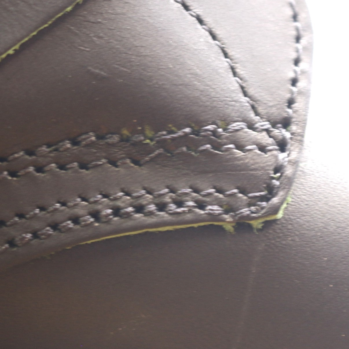 Close-up of a dark brown leather product showing detailed stitching and a slightly worn, frayed edge.